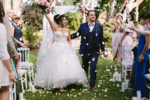 Les mariés heureux lors de la sortie de cérémonie laïque. Les invités lancent des pétales dans l'allée. Organisation mariage, conseil et accompagnement mariage , wedding planner