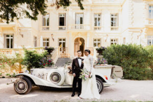 Photo de mariés devant la Château des trois Fontaines devant une ancienne voiture/ costume noir/ robe blanche